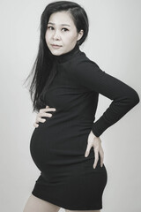 black and white photo of the young pregnant asian woman,Pregnancy health care preparing for baby concept.hugging belly isolated on gray background