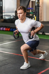 Handsome muscular man exercising with TRX straps in gym