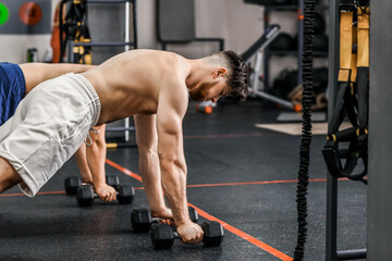 Fototapeta na wymiar Handsome muscular men exercising with dumbbells in gym
