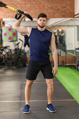 Fototapeta na wymiar Handsome muscular man exercising with TRX straps in gym