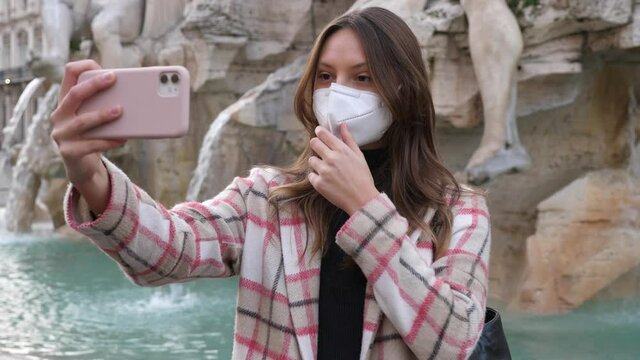 Ragazza turista scatta selfie con il suo smartphone davanti ai monumenti di Roma, ma prima si abbassa la mascherina dal viso, che la protegge dal coronavirus