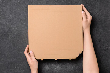 Hands with cardboard pizza box on dark background