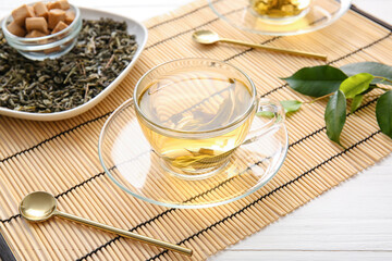 Cup of green tea, sugar and dry leaves on bamboo mat