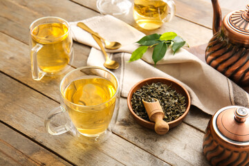 Cups of green tea and dry leaves on wooden table