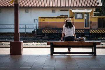 Fototapeta premium The back of the Asian woman tourist with hat is wearing a white and gray backpack while waiting for the train at the station