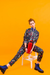 Stylish young girl posing with fire extinguisher on stepladder over orange background