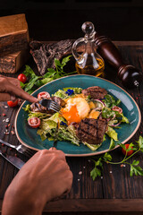 Eggs benedict with beef meat on a large white plate.. Traditional english breakfast with eggs Benedict, cherry tomato, lettuce. Benedict egg served on restaurant table background.