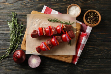 Cutting board with raw shish kebab on wooden background