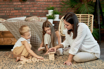 Mom and kids play squirl jenga tower. Woman girl and boy play family puzzle game. Family day off