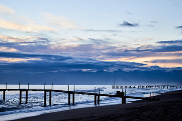 View from beach to water of sea, waves with white foam, pierce and sky with clouds in a nice evening.