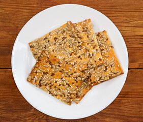 Flat flaky cookies with different seeds on dish, top view