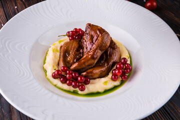 Stewed lamb tongues with red currants on a white plate. Restaurant serving.