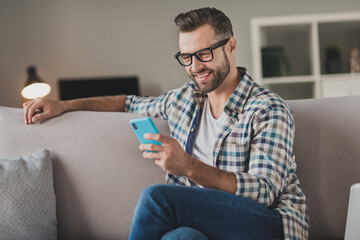 Photo of young cheerful man happy positive smile read browse internet cellphone chat type sms sit...