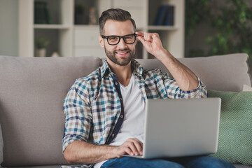 Photo of young handsome business man happy positive smile sit sofa home work distance browse laptop hand touch glasses