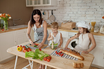 Children learn how to prepare a salad in the kitchen. Family day off, lunch with your own hands. Mom and young cooks