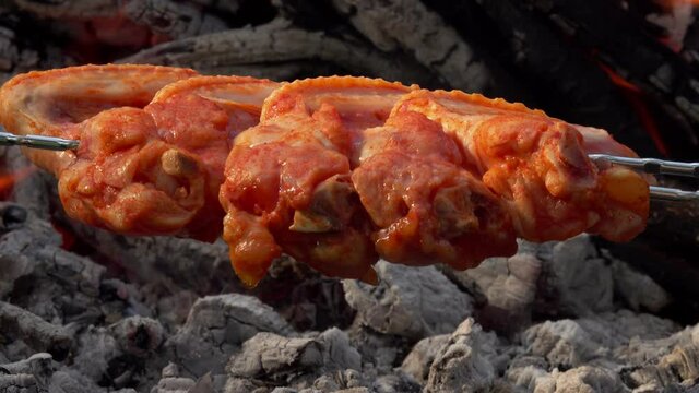 Close-up of the raw marinated chicken wings on the skewers frying above the open fire outdoors