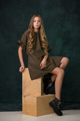 beautiful girl teenager blonde with long hair in a green dress posing in the studio sitting on wooden cubes