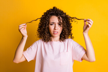 Photo portrait of unsatisfied female millennial keeping curls dry hair bad hairdo isolated on vivid yellow color background