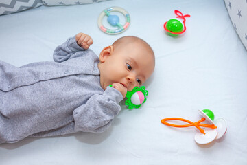 The newborn is lying on the bed with a hand in his mouth. Teething