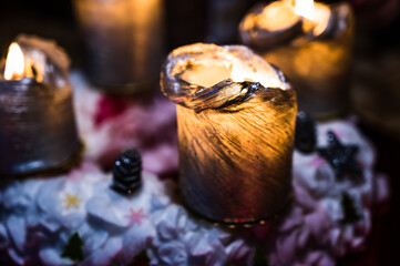 A closeup of burning golden-colored candles with Christmas decorations on a black background