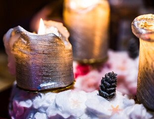 A closeup of burning golden-colored candles with Christmas decorations on a black background