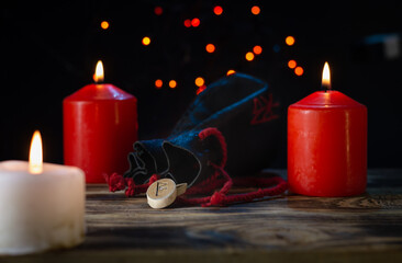 The rune Raido  is made ash tree trunk on a background of candles and a rune bag with a bokeh effect on a dark background