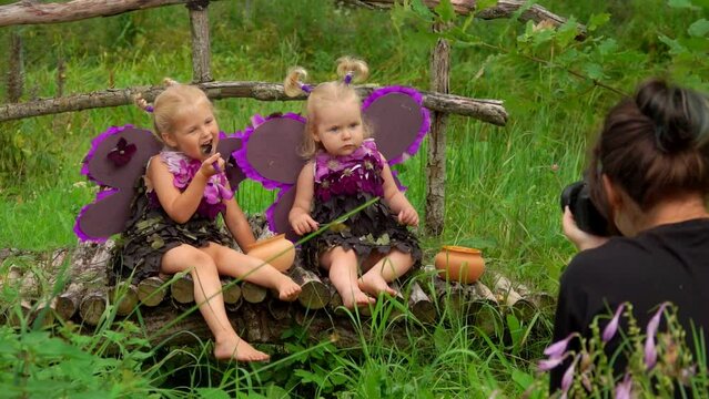 Female photographer is taking pictures of beautiful girls playing violet butterflies. Photoshoot of little girls wearing handmade butterfly wings