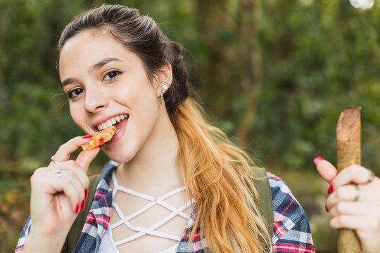Smiling Caucasian woman eating a healthy cereal snack bar - Portrait of a beautiful young woman eating a cereal bar in the forest.