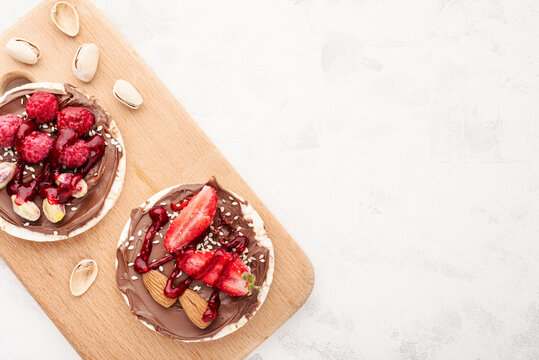 Rice cakes with chocolate-nut paste spread and raspberries with strawberries on cutting board with copy space