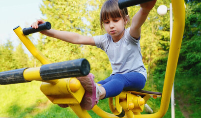 Portrait of beautiful young girl is engaged in sports on the playground for sports and strength training on simulators. Active healthy lifestyle of people concept. Horizontal image.