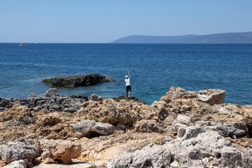 Izmir Turkey; Boy fishing on rocks at the seashore. 11 July 2020