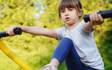 Beautiful young girl is engaged in sports on the playground for sports and strength training on simulators. Horizontal image.
