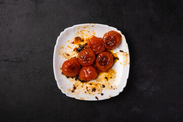 Baked minted cherry tomatoes on a white plate with traces of oil on a dark background, copy space, top view