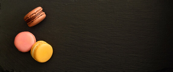 Macaroons colorful filled with cream on black serving plate flat lay or top view