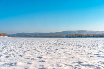 Winter icy landscape on a frozen snowy river, footprints visible in the snow