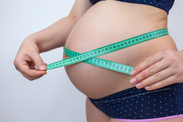 A pregnant woman measures her belly with a measuring tape