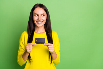 Portrait pf pretty cheerful person arms hold debit card look empty space isolated on green color...
