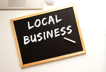 Text LOCAL BUSINESS written in chalk on a slate board. Office desk.