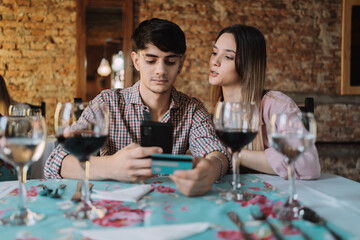Fototapeta premium Young smiling couple shopping online together - Happy couple enjoying dinner and paying the bill with a credit card
