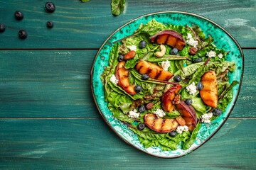 Delicious summer salad with grilled peaches, blueberry and goat cheese, Healthy food. Flat lay. Top...