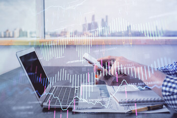 Double exposure of man's hands holding and using a digital device and forex graph drawing....