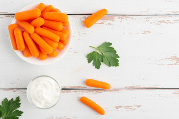 Small peeled pieces of carrot in plate on white wooden table. Top view. Copy space.