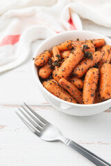 White bowl with small peeled pieces of cooked baby carrot on white textured wooden table