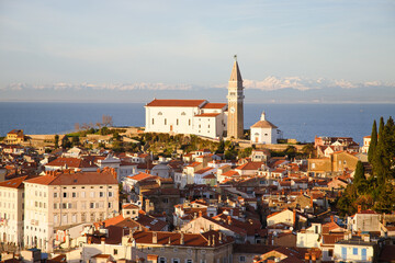 Red roofs of the historical center of old town Piran with main church against the sunset sky and...