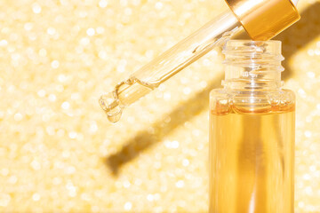 detail of pipette dropper with beauty serum on a bottle on a golden glitter shimmering background
