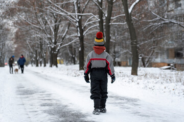 Back view child walks through snow-covered park. Alone boy