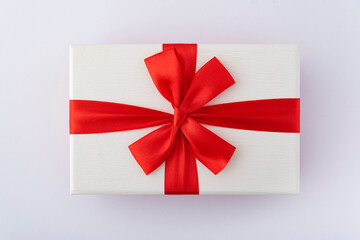 White box with red ribbon and bow on white background. Top view.