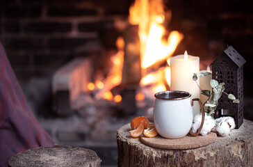 Cozy composition with a cup, candles and tangerines on a blurred background of a burning fireplace.