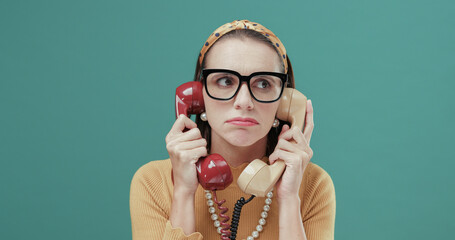 Woman holding two telephone receivers and feeling bored - obrazy, fototapety, plakaty