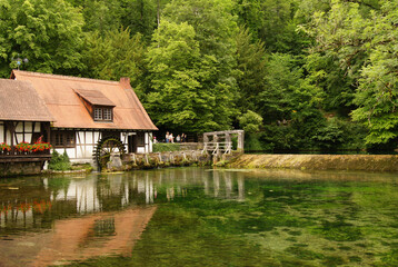 Obraz premium Scenic view of a historic hammer mill with a wooden water wheel at the Blautopf, a river source in Blaubeuren, Germany.